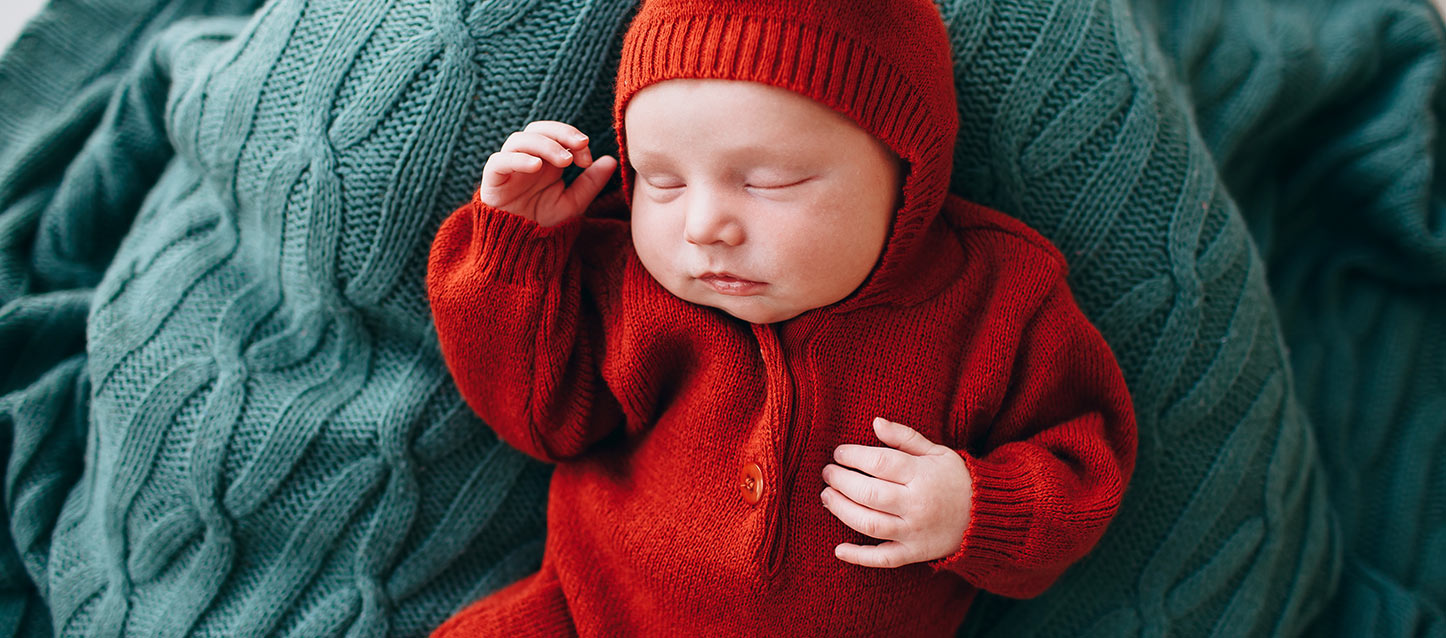 bebé com pijama com capuz vermelho, a dormir de barriga para cima sobre um travesseiro verde
