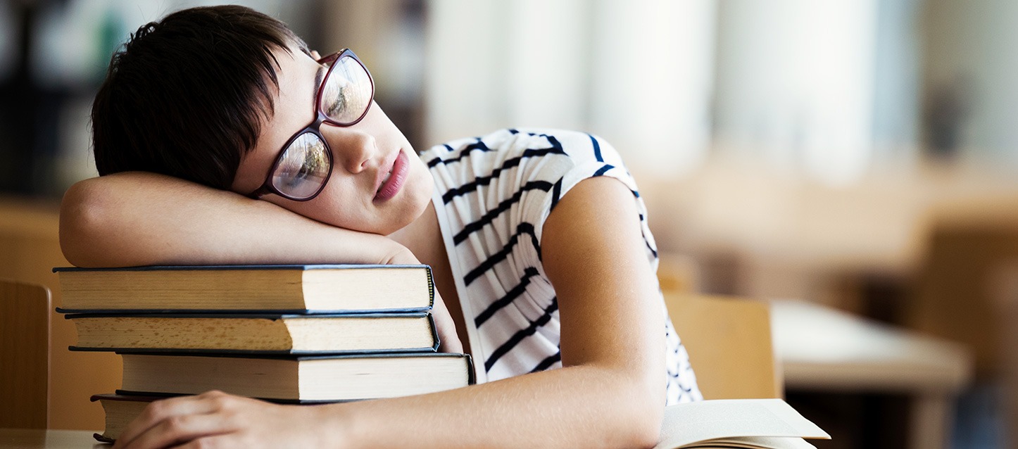 rapariga de cabelo curto moreno, com óculos, a dormir sobre livros na biblioteca