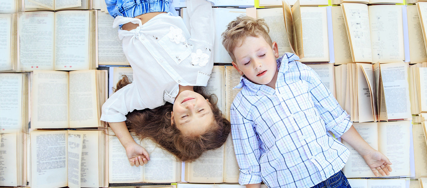 um menino e uma menina a dormirem em posições opostas sobre livros abertos