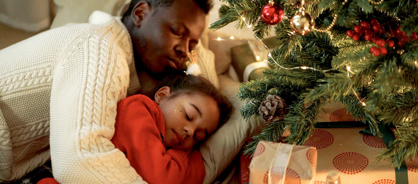 Pai e filha dormindo juntos ao lado da árvore de Natal com presentes.