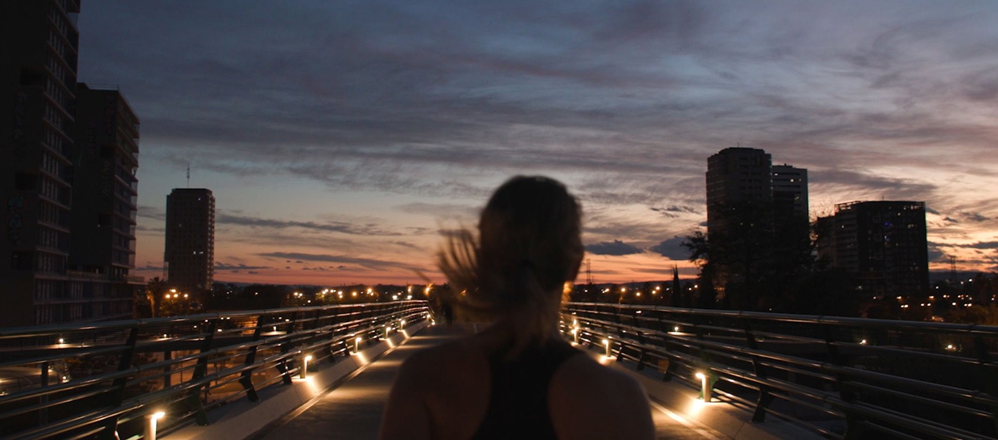 Mulher a correr ao amanhecer na cidade, atravessando uma ponte.
